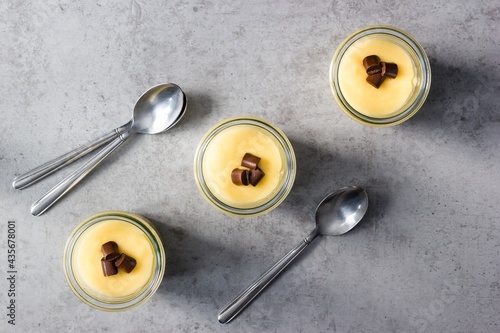 Three glasses of vanilla pudding arranged in an upwards pointing diagonal line on grey countertop photo