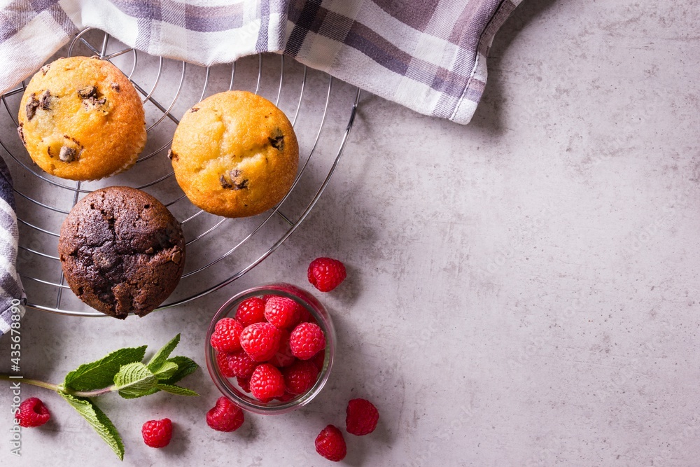Freshly baked cupcakes on cooling rack with napkin and raspberries and fresh mint aside on grey countertop Freshly baked cupcakes on cooling rack with napkin and raspberries and fresh mint aside on grey countertop