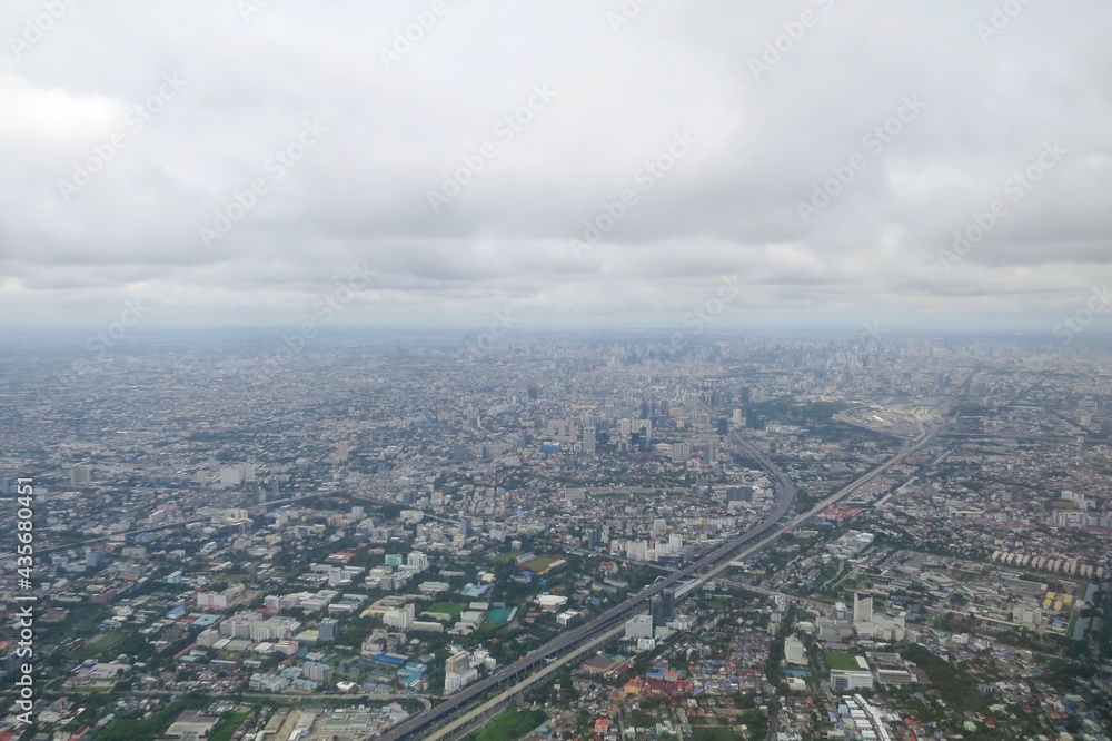 Fototapeta premium Aerial view of Bangkok, Thailand with building in big city, blue sky, and white cloud View from airplane's window. Soft focus. Transportation and landscape concept.