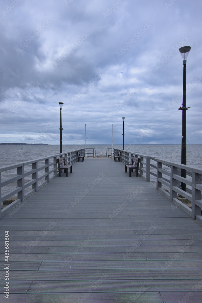 Central, vertical frame of a pier in Rewa located by Baltic Sea, with dramatic, stormy clouds above. 