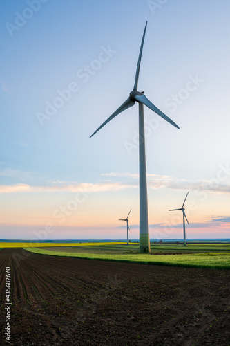 Wind turbines that produce sustainable green energy located on an agricultural field during a spring day at sunset. Vertical alignment.
