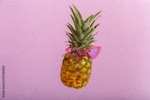 Pineapples creative faces in color sunglasses on pink color summer background. Tropical summer pineapple fruit levitating in pink sun glasses. Summer concept