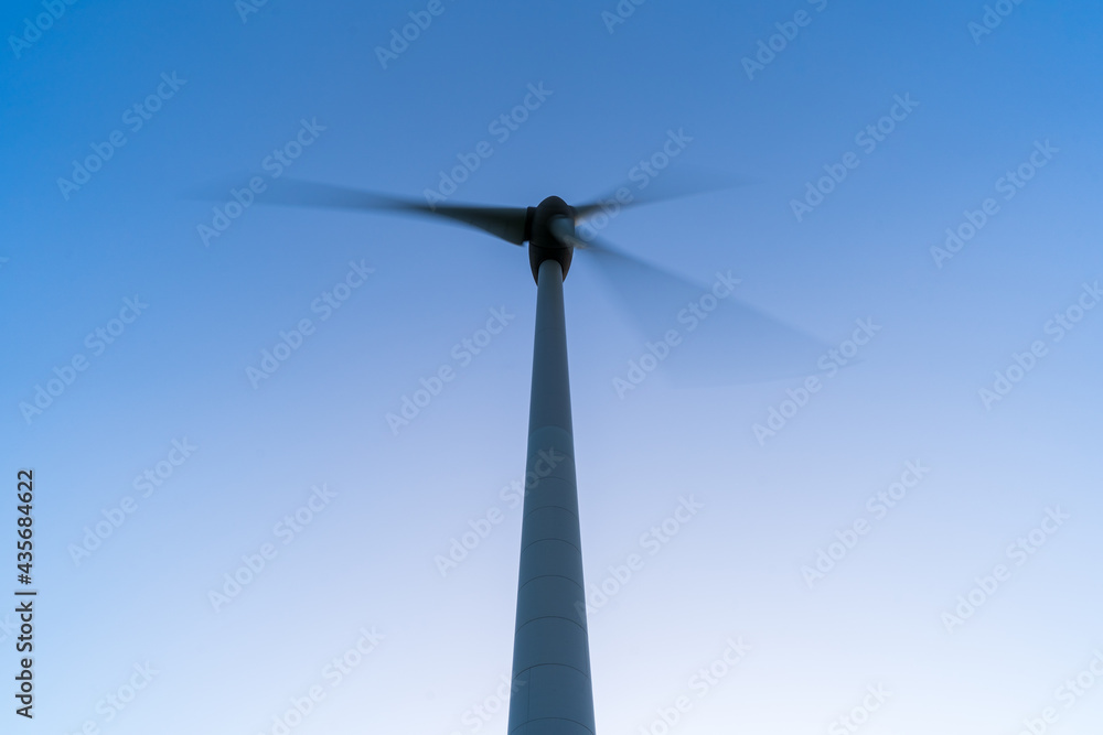 Bottom view of a wind turbine producing renewable green energy against the background of the blue sky. Copy space, motion blur. Bottom view of a wind turbine producing renewable green energy against the background of the blue sky. Copy space, motion blur.