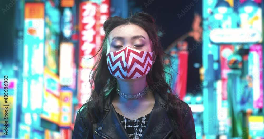 Portrait view of the brunette multiracial asian woman wearing protective face mask because of air pollution in the city or coronavirus pandemic looking confidently at the camera with neon background Portrait view of the brunette multiracial asian woman wearing protective face mask because of air pollution in the city or coronavirus pandemic looking confidently at the camera with neon background