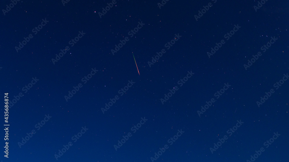Bright red-green meteor of Perseid flow in the night sky