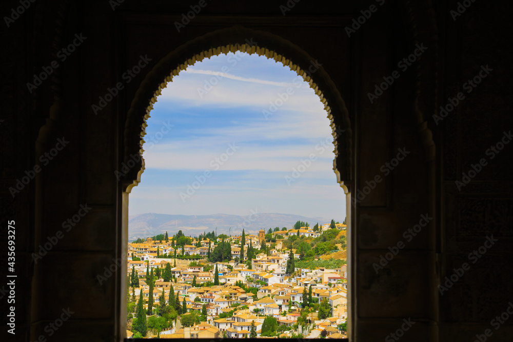 View through old stone window frame of medieval castle palace on spanish cityscape of mediterranean town - Alhambra, Granada, Spain