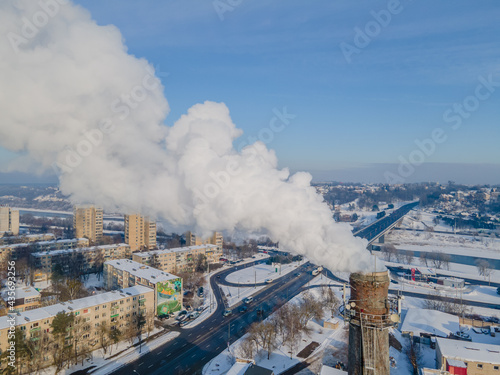 Pollution in a city. White smoke in winter coming from a huge industrial factory chimney located in the center of large city with residential areas around.