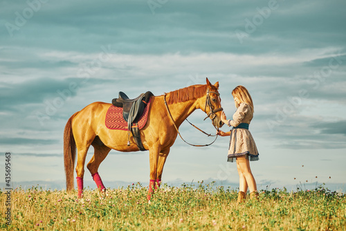 girl with horse in a field in the sunbeams of the sunset. beautiful sky above the horizon