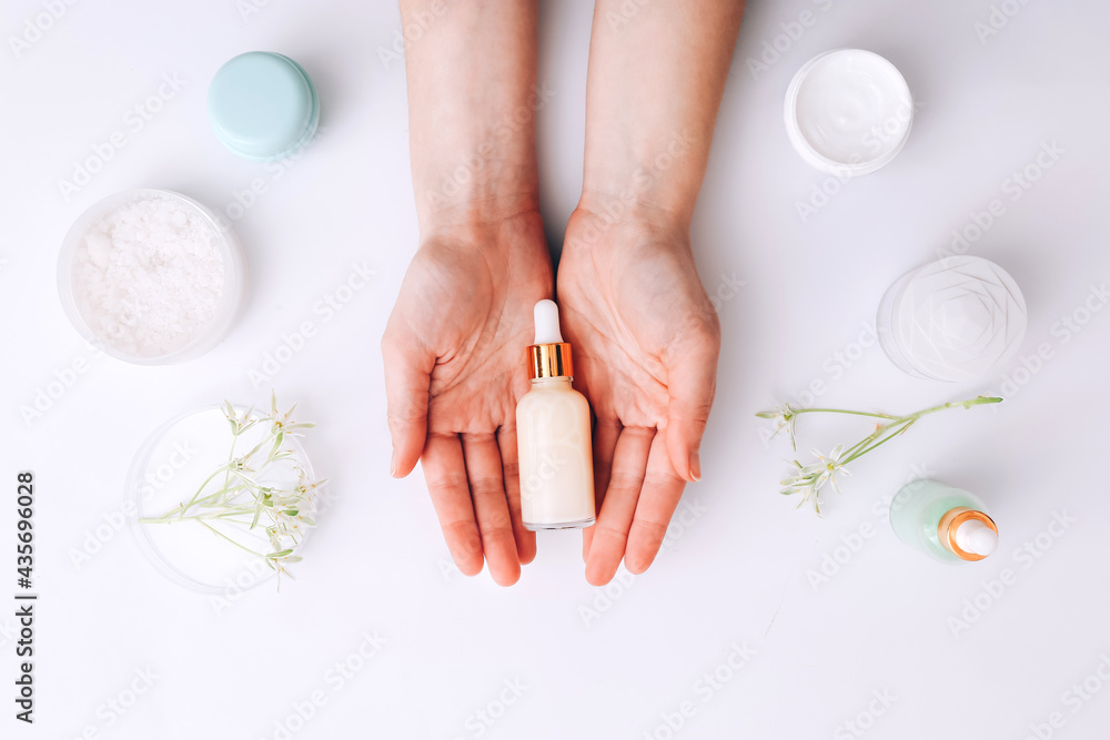 Woman holding bottle of cream over table with cosmetic products - obrazy, fototapety, plakaty 