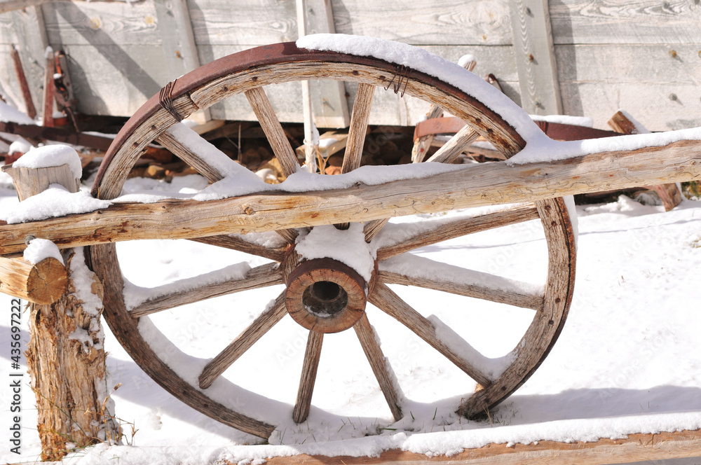 Old wagon wheel and wooden wagon in the snow outside of a small country town in Utah