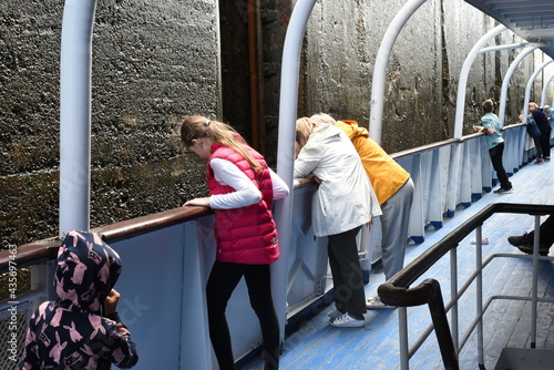 The ship descends in the lock. Wet concrete walls are visible. The people standing on the deck look down with interest.