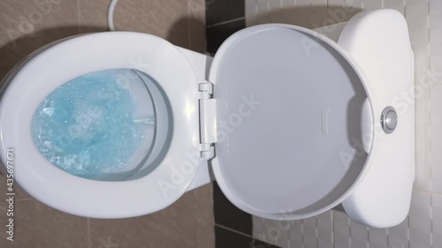 Hand and finger press on push button of flush toilet for water release to cleaning toilet bowl in bathroom. Blue water swirls flow for cleanup and hygiene of toilet bowl. About flushing toilet concept