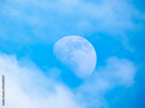 An incomplete moon in the afternoon against a blue sky partially hidden by a white cloud