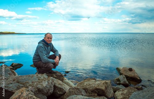 A middle-aged man admires the landscape of a lake with clouds, blue skies and reflections in the water. Kakhovskoe reservoir, Ukraine. photo