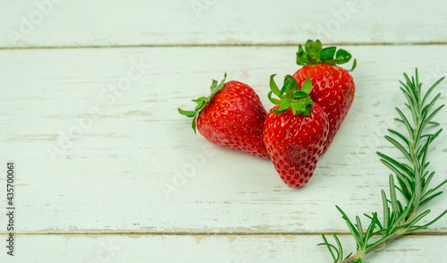 Top view of three strawberries on white wooden background.