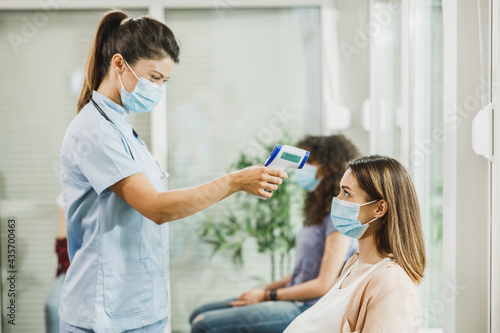 Nurse Measuring Temperature In Waiting Room During Covid-19 Pandemic