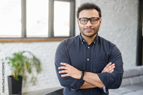 Konstfotografi Ambitious hindu man in smart casual shirt stands with arms crossed in contemporary office space and looks at camera, portrait of purposeful indian businessman, ceo indoor