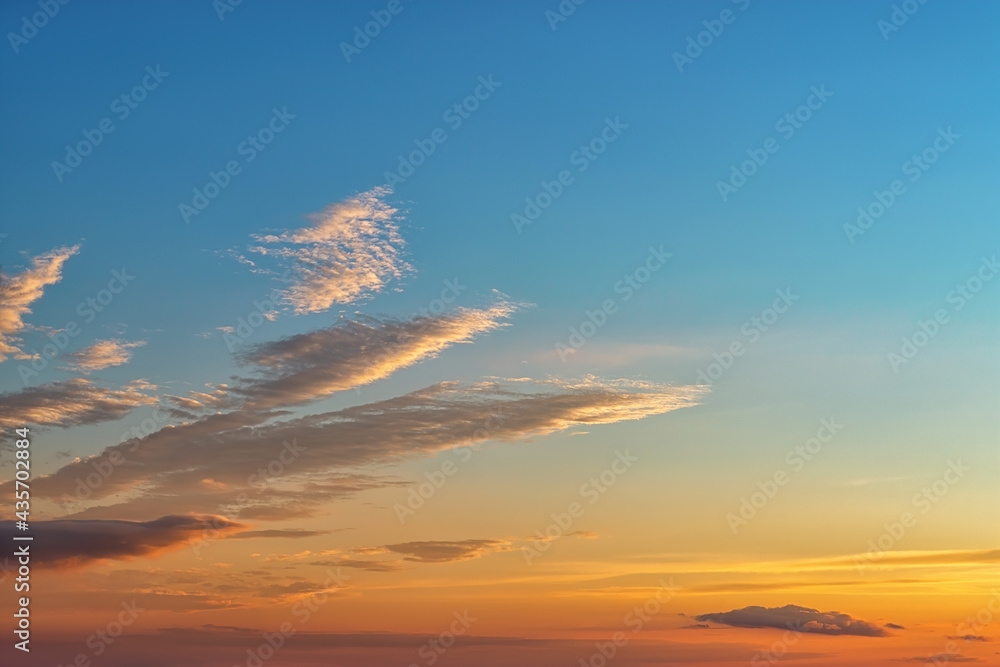 Calm golden blue sunset sky with few long clouds at left. The rays of the setting sun gilded the clouds and the sky above the horizon. Summer evening sky at golden hour. Weather forecast