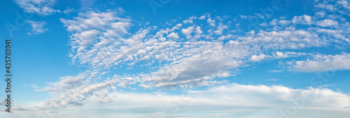 Fluffy cirrus clouds float slowly high in the azure blue sky on a sunny day. Panoramic skyscape of many small white clouds are scenic scattered across the sky. Weather and meteorology. Wide banner