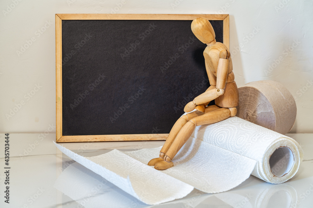 Wooden figure sit on a roll of toilet paper. Concept of the problem with digestion.