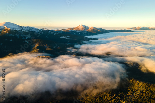 Aerial view of vibrant sunrise over white dense fog with distant dark Carpathian mountains on horizon.