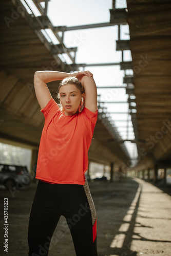 Portrait of fit and sporty young woman doing stretching under a bridge.