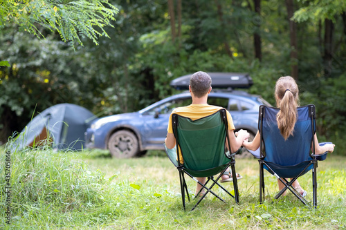 Back view of a happy couple sitting on chairs at campsite relaxing together. Travel, camping and vacations concept.
