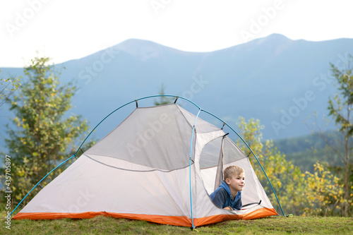 Hiker child boy sitting inside a tent in mountain campsite enjoying view of nature.