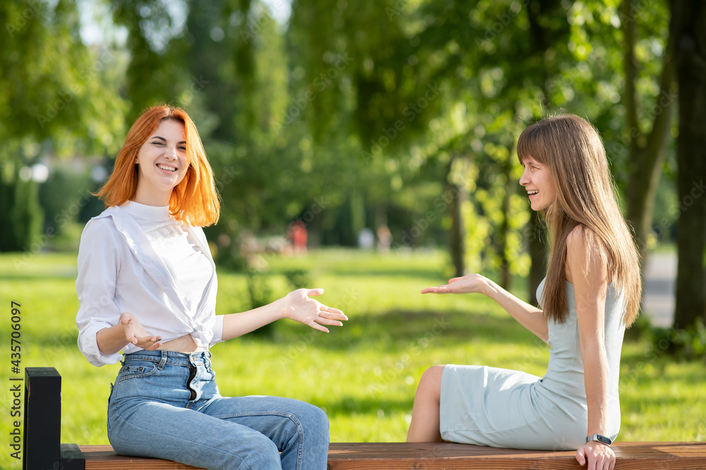 Two young women friends sitting on a bench in summer park and talking having an argument. Two young women friends sitting on a bench in summer park and talking having an argument.