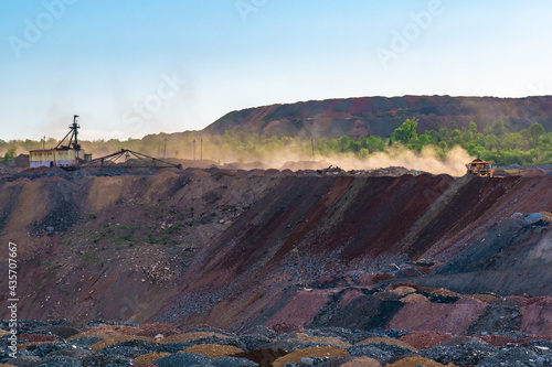 A dump truck transports rock in a quarry. A yellow dumper transports stones in a opencast mine, forming huge clouds of dust, illuminated by sunlight.
