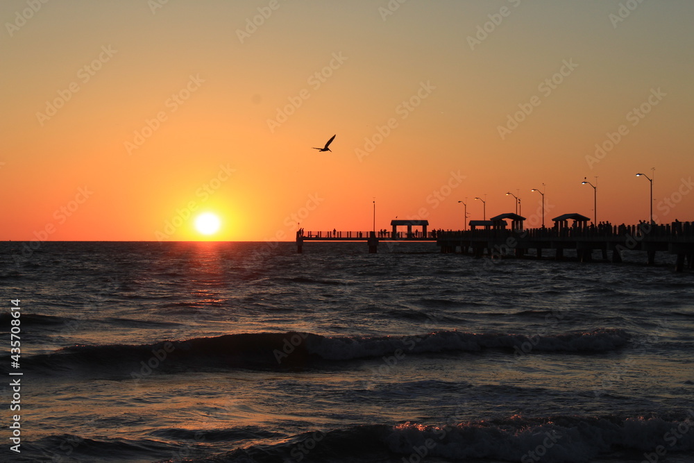 Fishing pier at the beach with the sun on the horizon at sunset