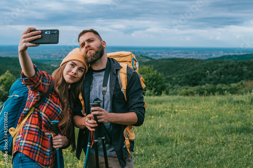 Hikers taking selfie with a smartphone and using trekking poles while wearing backpacks