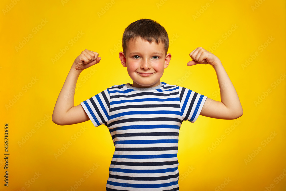 A child boy showing his hand biceps muscles strength on yellow background. Smart kid showing his arms muscles with fists A child boy showing his hand biceps muscles strength on yellow background. Smart kid showing his arms muscles with fists