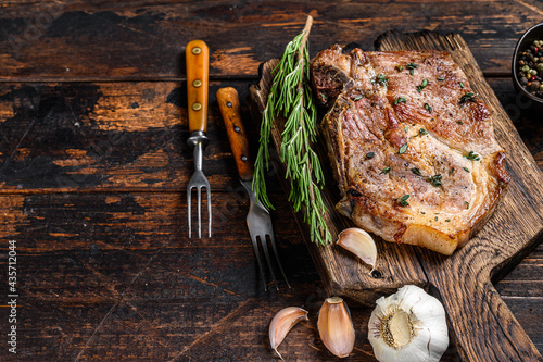 Roasted pork chop steak on a cutting board. Dark wooden background. Top view. Copy space