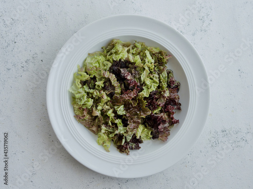 fresh green salad in white plate on white background, top view