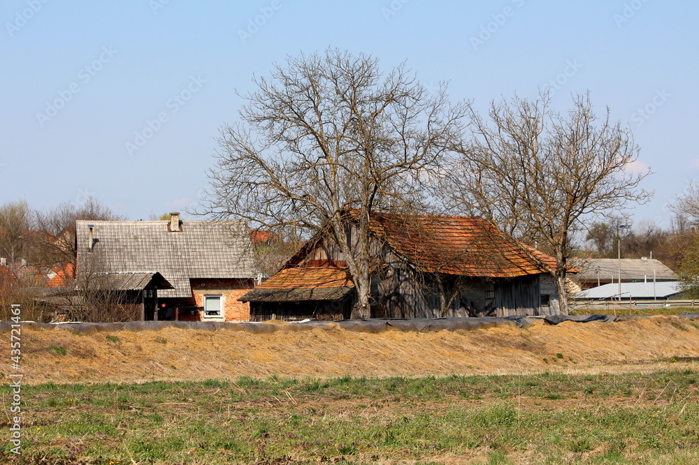 Temporary flood protection wall made of box barriers and sandbags covered with thick geotextile fabric and nylon protecting red brick family house and large wooden barn covered with old dilapidated ro