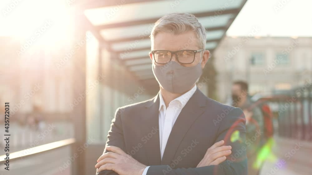 Close up portrait of happy Caucasian handsome man in suit standing in city looking at camera at bus station in sunshine wearing mask on face. Male in glasses outdoors in town, coronavirus pandemic Close up portrait of happy Caucasian handsome man in suit standing in city looking at camera at bus station in sunshine wearing mask on face. Male in glasses outdoors in town, coronavirus pandemic