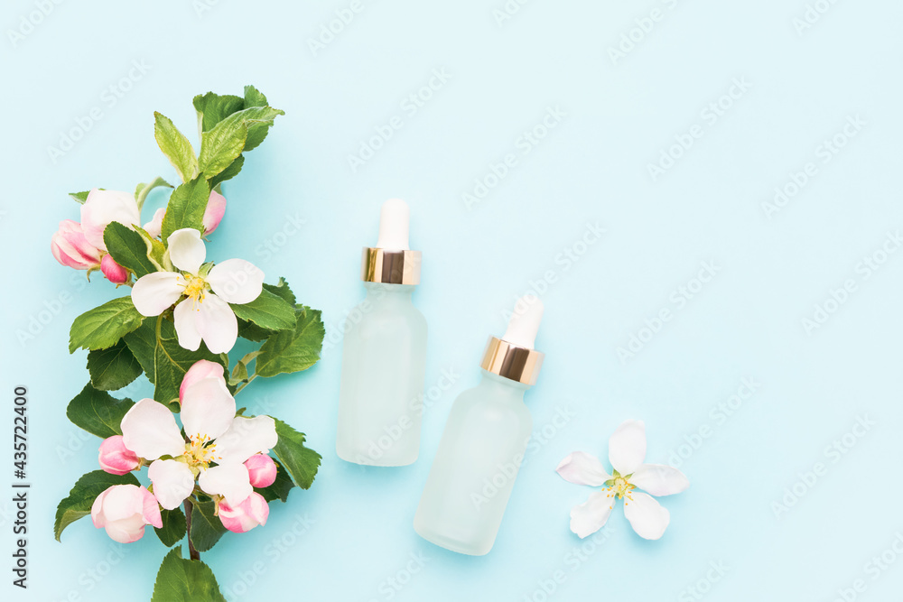 Glass dropper bottles for medical and cosmetic use and apple tree blossom flowers on a light blue background. SPA concept Glass dropper bottles for medical and cosmetic use and apple tree blossom flowers on a light blue background. SPA concept