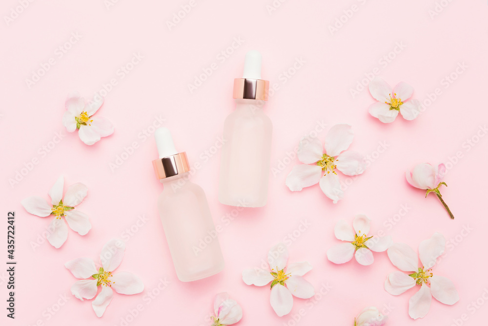 Glass dropper bottles for medical and cosmetic use and apple tree blossom flowers on a pink background. SPA concept Glass dropper bottles for medical and cosmetic use and apple tree blossom flowers on a pink background. SPA concept