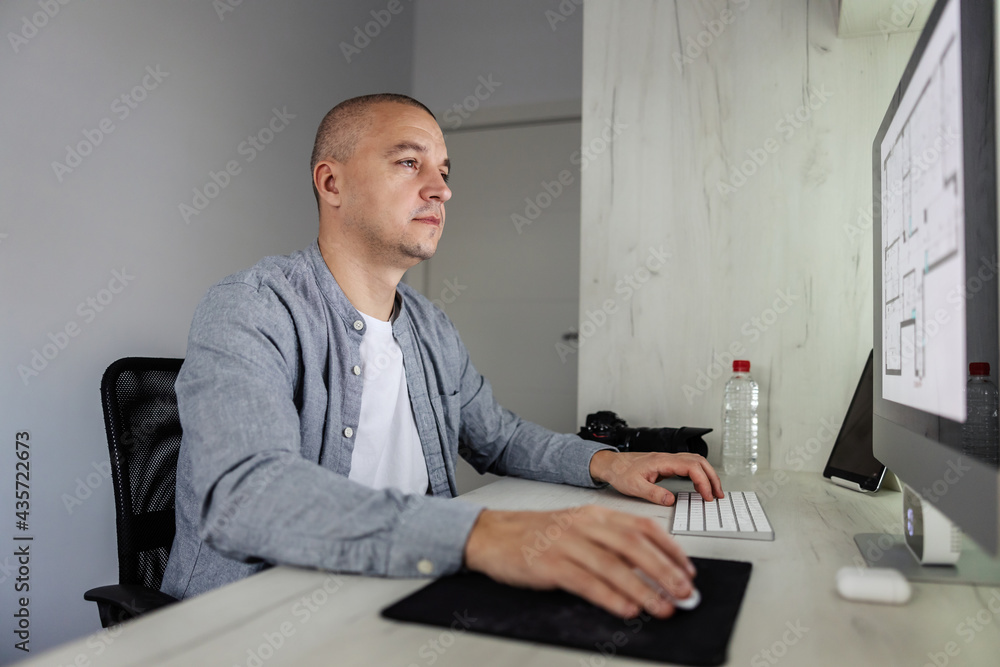 Dedication to work. A man in casual clothes sits in front of a desktop computer and does some to do tasks. He is in an isolated small room office and concentrating on work. Cyberspace, love my job