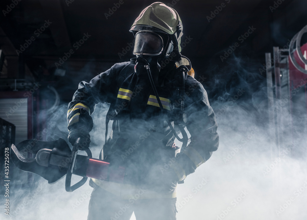 Obraz premium Portrait of a fireman wearing firefighter turnouts and helmet. Dark background with smoke and blue light.