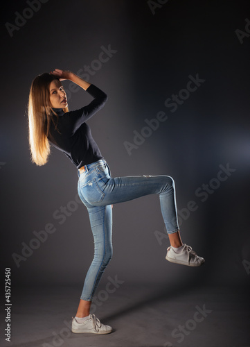Side full-body portrait of a young female model in black top and jeans posing with one leg in front