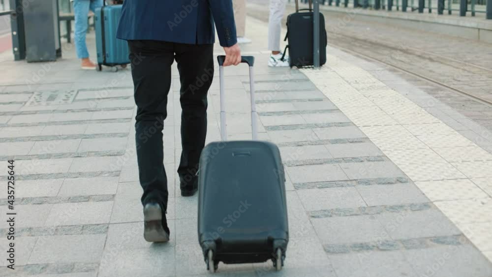 Rear of unrecognizable male in suit walking in town on street with suitcase going on trip. Man walk outdoors with luggage bag, travelling, travel time, vacation, business trip, Close up. Back view Rear of unrecognizable male in suit walking in town on street with suitcase going on trip. Man walk outdoors with luggage bag, travelling, travel time, vacation, business trip, Close up. Back view