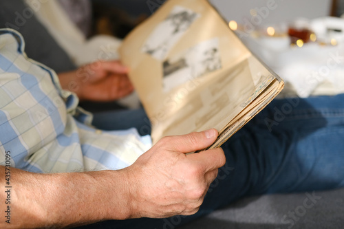 an elderly man looks through an album with old photographs  a concept of memories of youth  childhood  remembering his life  relatives  family connection of generations