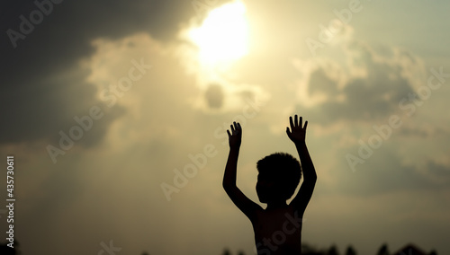 Little boy raising hands over sunset sky, enjoying life and nature. Happy Kid on summer field looking on sun. Silhouette of male child in sunlight rays. Fresh air, environment concept.