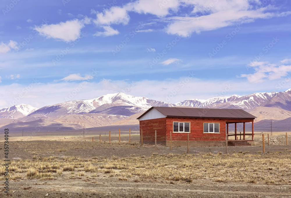 A house in the Altai Mountains. A lonely building in the Chui steppe in spring against the background of the snow-covered Kurai ridge under the blue sky. Siberia, Russia