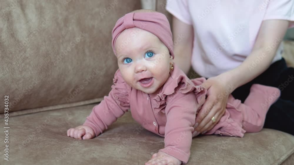 A baby girl with blond hair and blue eyes in pink clothes lies on her tummy and swings in different directions. Child development in the first year of life A baby girl with blond hair and blue eyes in pink clothes lies on her tummy and swings in different directions. Child development in the first year of life