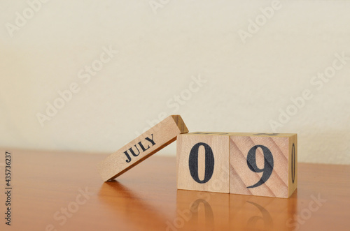 July 9, Date design with calendar cube on wooden table and white background.