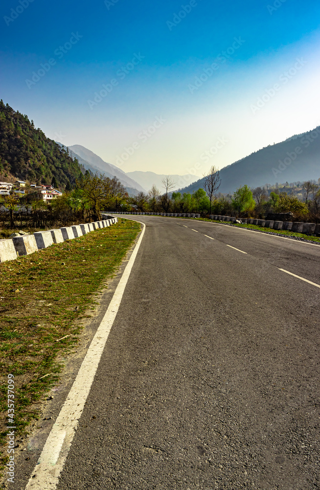 tarmac road leading to the misty mountain valley with blue sky at morning from flat angle