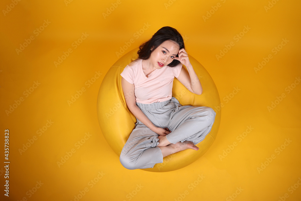 Beautiful young south east Asian woman sits on a yellow beanbag seat orange yellow color background pose fashion style elegant beauty mood expression rest relax think emotion top view Beautiful young south east Asian woman sits on a yellow beanbag seat orange yellow color background pose fashion style elegant beauty mood expression rest relax think emotion top view